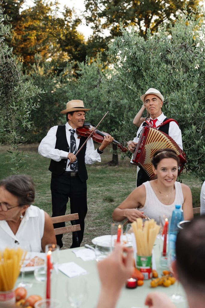 Italienische Musiker mit Akkordeon und Gesang unterhalten die Gäste während einer Pizza-Party im Olivenhain.