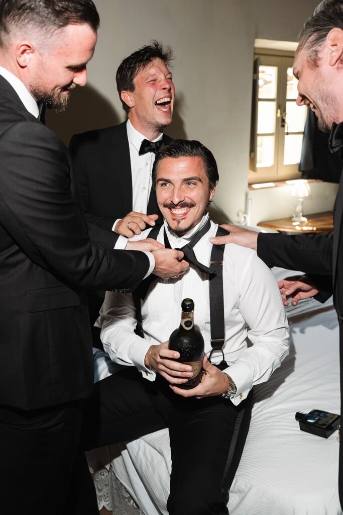 Bräutigam Erik lacht gemeinsam mit seinen Groomsmen beim Ankleiden vor der Hochzeit in der Toskana.