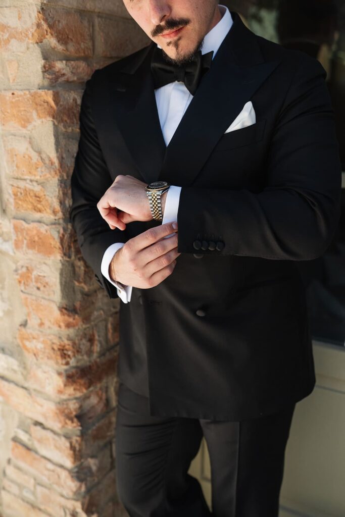 Detailaufnahme eines Bräutigams im schwarzen Smoking mit Fliege und weißem Hemd bei einer Hochzeit in der Toskana.