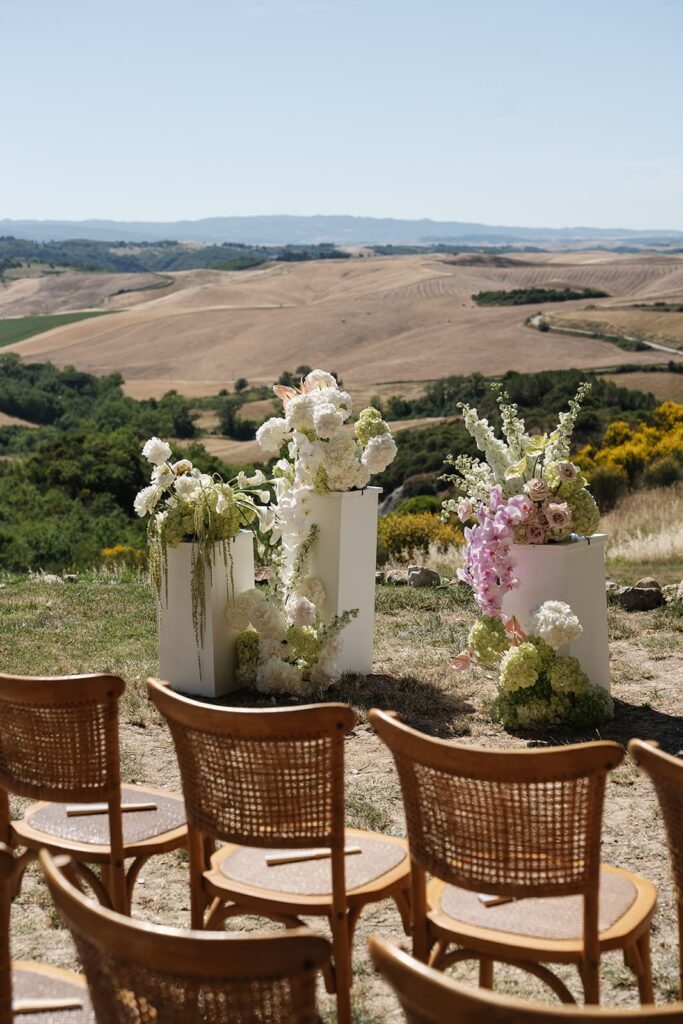 Elegantes Outdoor-Trauungssetting mit floralen Arrangements und Stühlen vor der weiten Hügellandschaft rund um Volterra.