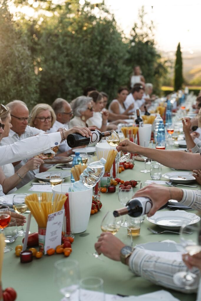 Italienisch dekorierte Dinner-Tafel mit frischen Tomaten, Pasta, Gläsern und weißen Tellern bei einer Pizza-Party in der Toskana.