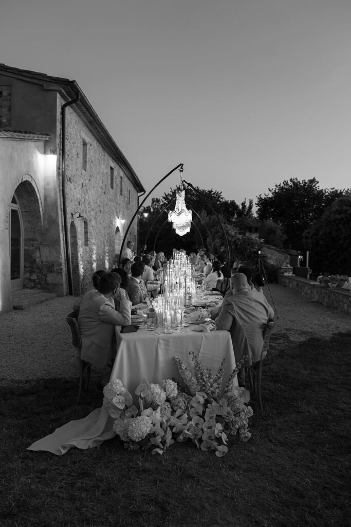 Schwarz-Weiß-Aufnahme einer festlich gedeckten Hochzeitstafel mit Gästen im Außenbereich eines italienischen Landhauses.