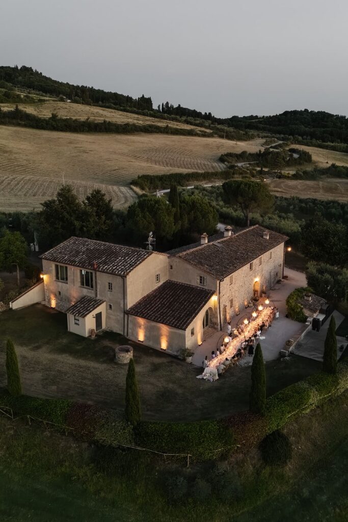 Drohnenaufnahme eines rustikalen italienischen Landhauses mit Außenbereichen in der hügeligen Landschaft der Toskana.