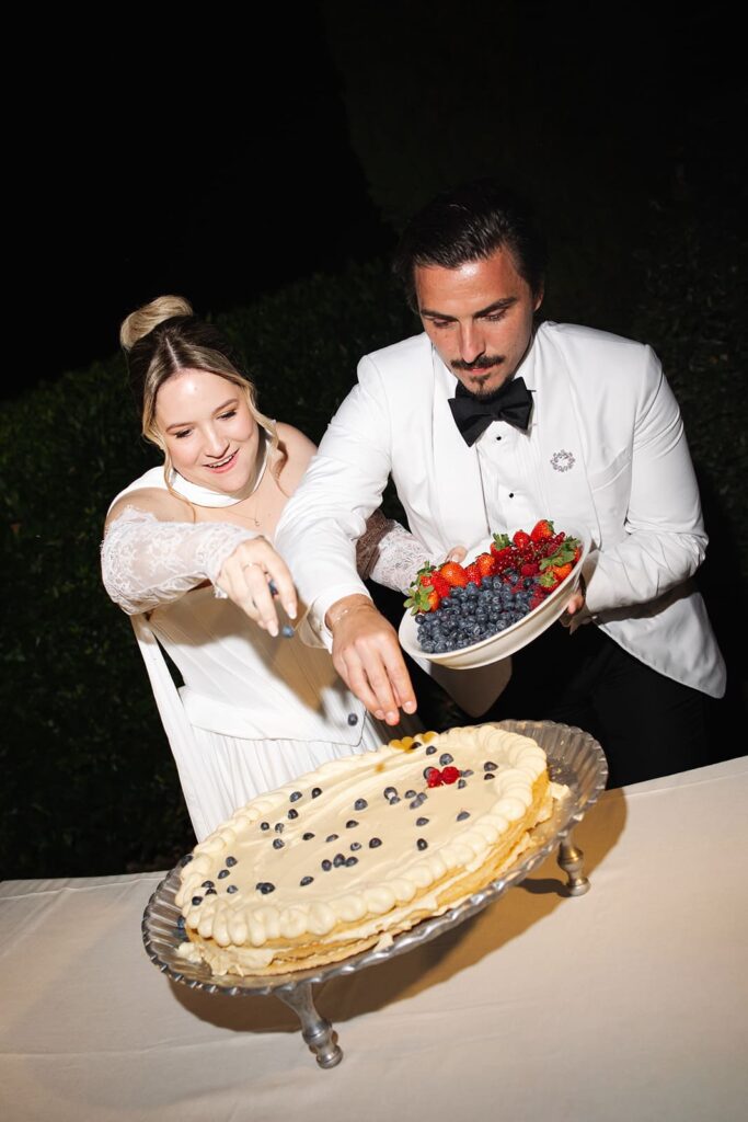 Sophie und Erik dekorieren gemeinsam ihre italienische Hochzeitstorte mit Creme und frischen Früchten.