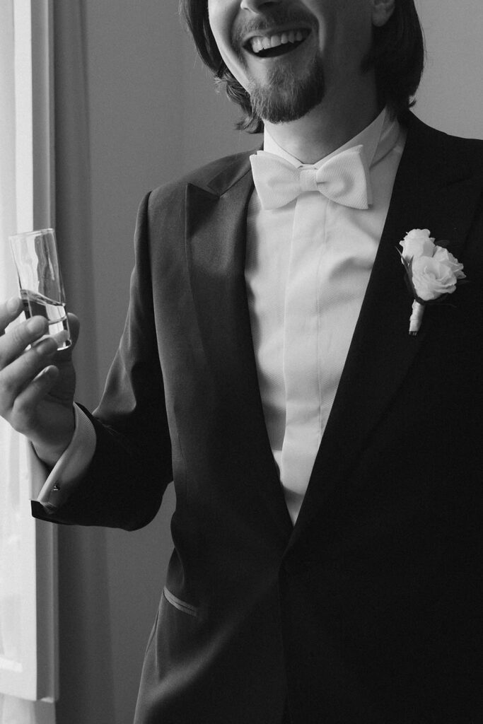 Bräutigam Szymon im eleganten schwarzen Smoking mit weißer Fliege und Ansteckblume beim Getting Ready.