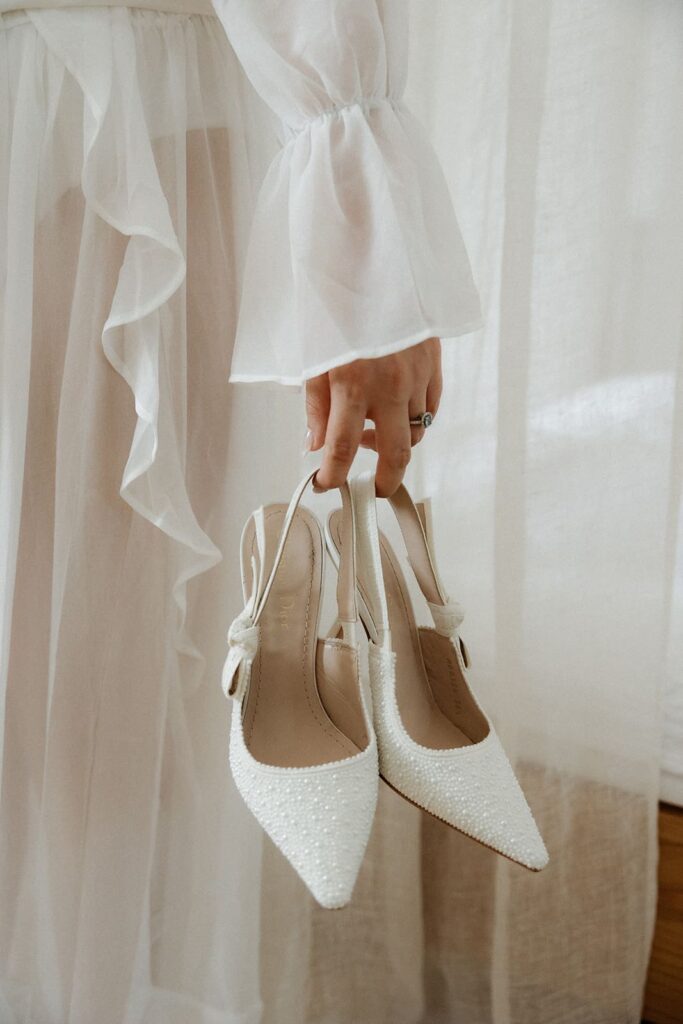 Elegante weiße Brautschuhe mit Schleifendetails während des Getting Readys der Braut Sali.