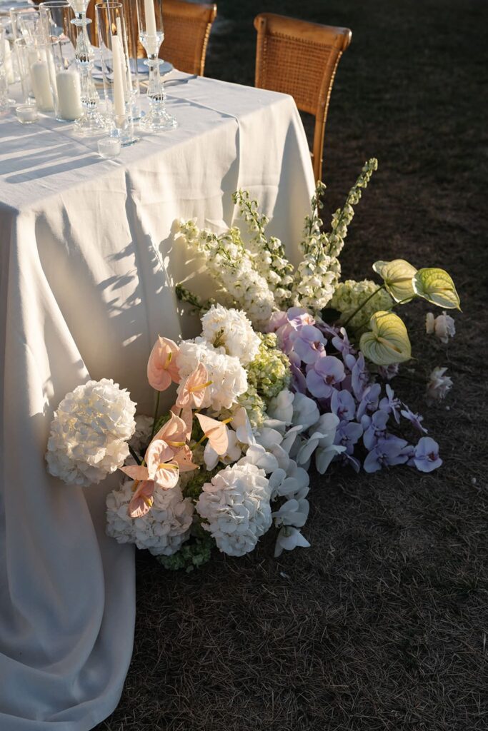 Üppiges Blumenarrangement in Weiß, Rosa und zartem Violett neben einer hell gedeckten Hochzeitstafel in der Toskana.