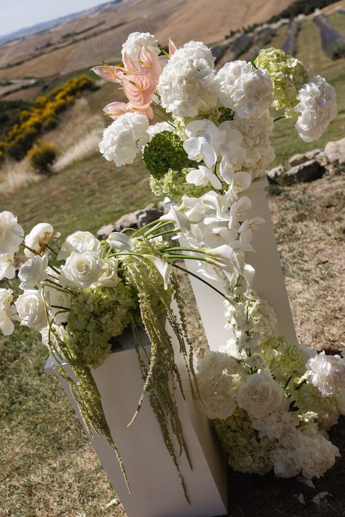 Üppiges Blumenarrangement mit weißen, rosafarbenen und zartvioletten Blüten auf einem hellen Sockel bei einer freien Trauung in der Toskana.