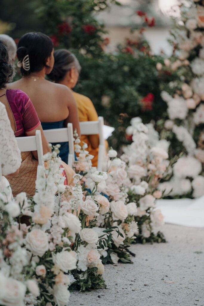 Hochzeitsgäste zwischen üppigen Blumenarrangements in Weiß, Creme und Apricot bei einer eleganten Trauung.