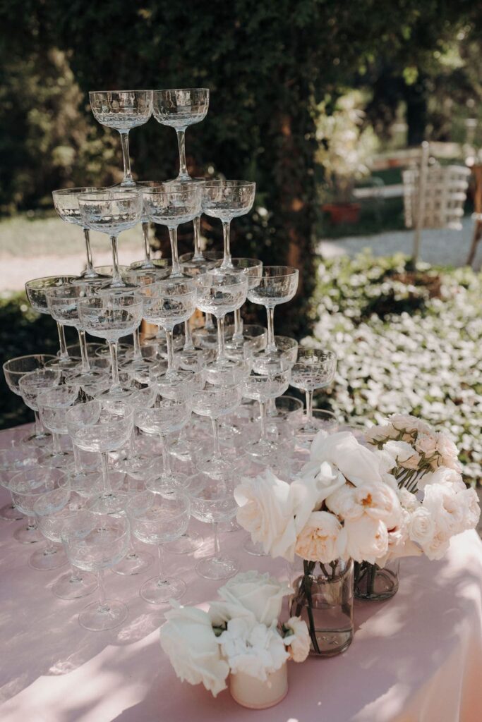 Elegante Champagnerpyramide aus gestapelten Gläsern mit floraler Dekoration beim Hochzeitsempfang im Freien.