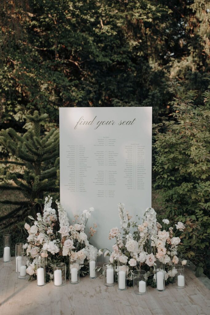 Hochzeitsschild mit schlichter Typografie, umgeben von üppigen weißen und cremefarbenen Blumenarrangements.