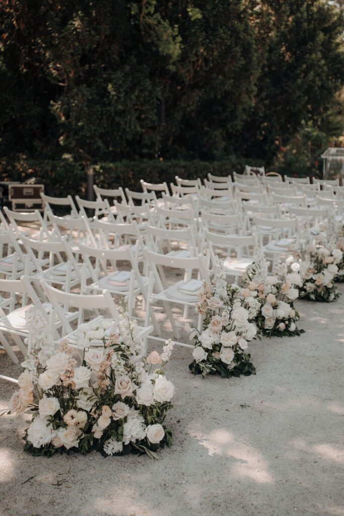 Elegante Trauung im Schloss Schönau mit weißen Stühlen und üppigen Blumenarrangements in Creme und zarten Apricottönen.